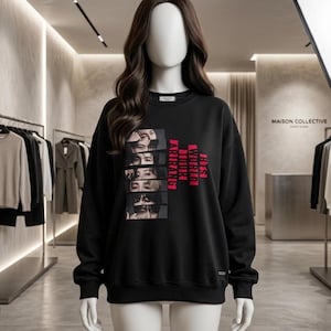Op de afbeelding: Een zwart sweatshirt met lange mouwen en een grafische print van zes individuele portretten die verticaal aan de linkerkant zijn gestapeld. Rechts van de portretten staat de tekst BTS WORLD TOUR ARIRANG in dikke, verticale, felroze hoofdletters.