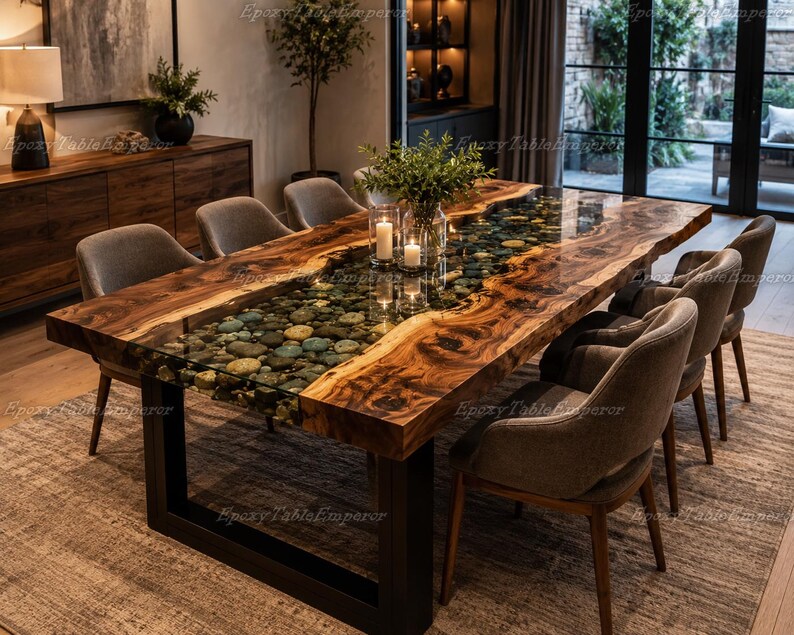May include: A rectangular dining table featuring a live edge walnut wood slab with a central river section filled with smooth, multi-colored river stones encased in clear epoxy resin, supported by a sturdy black metal U-shaped frame base.