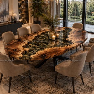 Op de afbeelding: Een ovale eettafel met een houten blad met natuurlijke randen en een centraal rivierachtig inlegwerk van heldere epoxyhars gevuld met donkere stenen, op een zwart metalen onderstel, omringd door acht gestoffeerde stoelen in neutraal beige.