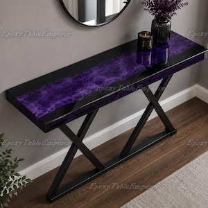 May include: A rectangular console table featuring a glossy black finish with a central, wavy inlay of deep purple epoxy resin. The table is supported by a black metal base with two intersecting X-shaped legs. A black candle and a vase are on top.