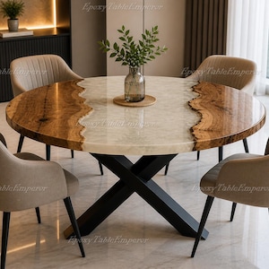 Puede incluir: Una mesa de comedor redonda con una tapa de madera y resina epoxi. La mesa presenta un diseño de veta de madera natural en los bordes y un centro de resina epoxi de color claro. Tiene una base de metal negro y está rodeada de sillas tapizadas beige.