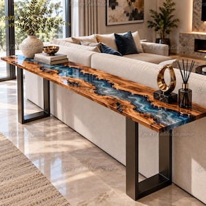 Puede incluir: Una consola rectangular larga que presenta una losa de madera natural con una incrustación central de resina epoxi azul y blanca similar a un río. La mesa se apoya en dos patas de metal negro en forma de U y tiene un acabado brillante y liso.