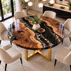 May include: A round dining table featuring a natural wood slab with a glossy black epoxy resin centre inlay filled with smooth river stones and gold leaf accents. The table is supported by a gold-coloured metal base with a cross-leg design.