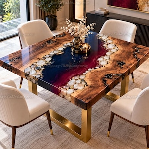 May include: A square dining table featuring a natural wood slab with a central resin river in deep blue and magenta hues, accented by embedded white stones. The table is supported by gold-toned metal legs and surrounded by four cream-colored chairs.