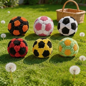 Puede incluir: Seis coloridos balones de fútbol de peluche descansan sobre hierba verde. Las bolas presentan varias combinaciones de colores, incluyendo negro y naranja, rosa y blanco, negro y blanco, rojo y negro, amarillo y negro, y verde y naranja. Una cesta de mimbre está en el fondo.