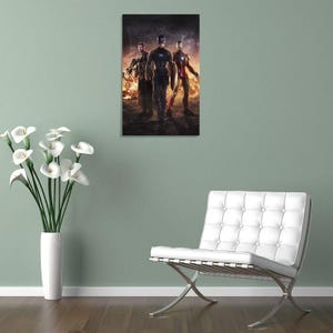 May include: A framed print featuring three superheroes: Captain America, Iron Man, and Thor, standing in front of a fiery background. Captain America is in the center, wearing a blue and white suit. Iron Man is on the right, in a red and gold suit.