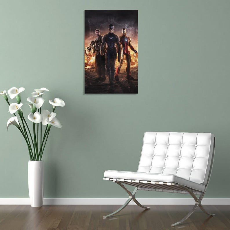 May include: A framed print featuring three superheroes: Captain America, Iron Man, and Thor, standing in front of a fiery background. Captain America is in the center, wearing a blue and white suit. Iron Man is on the right, in a red and gold suit.