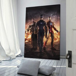 May include: A canvas print featuring three superheroes: Captain America, Iron Man, and Thor, standing in front of a fiery background. Captain America holds his shield, while Iron Man's suit glows red and gold. Thor is armed with a weapon.
