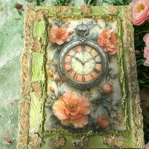 May include: A rectangular decorative box featuring a central pocket watch illustration surrounded by peach-colored flowers. The frame is textured in light green with gold-toned floral accents. The watch face displays Roman numerals.