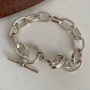 May include: A silver chain link bracelet featuring polished oval links and a circular toggle clasp. The toggle bar is clearly engraved with the number 925, indicating the silver content. The bracelet is constructed from interconnected metal loops.