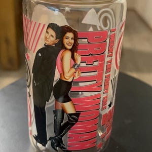 May include: A clear glass jar with a bamboo lid, decorated with a graphic from the film "Pretty Woman." The design shows the actors and the movie title in pink and red. The jar is cylindrical and suitable for drinks.