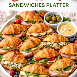 May include: A white platter filled with mini croissant sandwiches, featuring various fillings like sliced ham, cheese, and creamy salads. The platter includes two small white bowls containing green olives and a yellow dipping sauce, garnished with fresh berries.