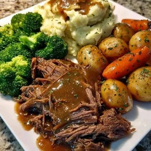 May include: A plate of food featuring shredded beef topped with brown gravy, a mound of mashed potatoes with gravy, steamed green broccoli florets, roasted baby potatoes, and glazed orange carrots, all arranged on a white square plate.