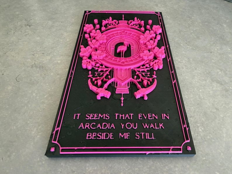 May include: A rectangular black plaque featuring a raised hot pink relief design. The top section displays a central flamingo silhouette surrounded by intricate floral patterns and geometric borders. The text reads: IT SEEMS THAT EVEN IN ARCADIA YOU WALK BESIDE ME STILL.