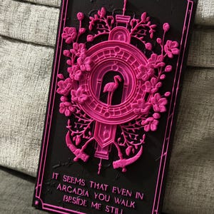 Peut inclure: Plaque rectangulaire noire avec un motif rose en relief représentant un flamant rose, des fleurs et le texte "IT SEEMS THAT EVEN IN ARCADIA YOU WALK BESIDE ME STILL." Le motif a une bordure décorative.