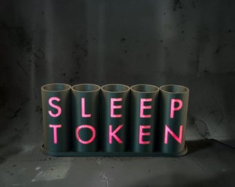 May include: A set of five dark gray cylindrical containers arranged in a row on a matching base. Each container features a cutout letter in bright pink, spelling out the words SLEEP TOKEN across the front of the five individual units.