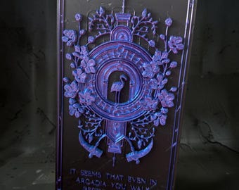 May include: A rectangular plaque with a dark base and iridescent purple relief detailing. The center features a flamingo inside a circular frame surrounded by floral motifs. The text reads: IT SEEMS THAT EVEN IN ARCADIA YOU WALK BESIDE ME STILL.