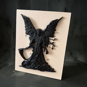 May include: A rectangular light beige plaque featuring a raised, three-dimensional black relief of a hooded figure with large, detailed wings. The figure holds a scythe in one hand and a small star-shaped object in the other, set against a textured background.