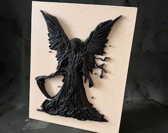 May include: A rectangular light beige plaque featuring a raised, three-dimensional black relief of a hooded figure with large, detailed wings. The figure holds a scythe in one hand and a small star-shaped object in the other, set against a textured background.