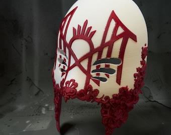 May include: A cream-colored mask featuring intricate, raised dark red filigree patterns along the lower edges and a prominent, symmetrical dark red geometric design across the forehead and eye areas, with cutouts for the eyes and nose.
