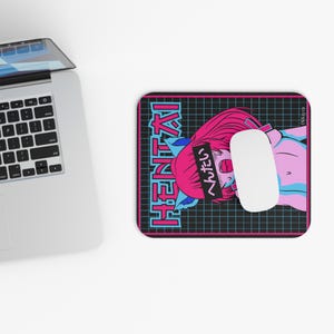 May include: A rectangular mouse mat with a black grid pattern and the word "HENTAI" in teal and pink. The mat features a pink-haired anime character with a black headband and Japanese text. A white mouse rests on the mat.