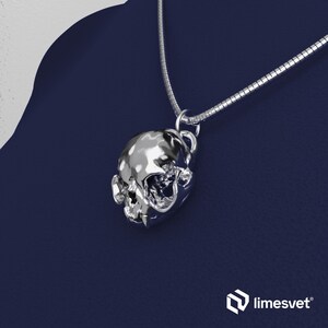 May include: A silver skull pendant on a silver chain, set against a dark blue backdrop. The skull has intricate detailing and a shiny, reflective finish. The chain is fine, and the pendant is the main focus of the image.