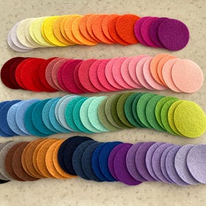 May include: Rows of felt circles in a rainbow of colours, from pale pastels to rich reds, oranges, greens, and purples. The circles are neatly arranged, demonstrating a wide variety of shades. The felt circles are arranged in a visually pleasing display.