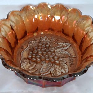 May include: A vintage iridescent orange glass bowl with a grapevine design. The bowl has a scalloped edge and is perfect for serving fruit or snacks.