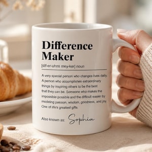 May include: A white ceramic mug featuring black printed text that defines the term Difference Maker. The text includes a phonetic pronunciation, a descriptive paragraph, and the name Sophia printed in a cursive script at the bottom.