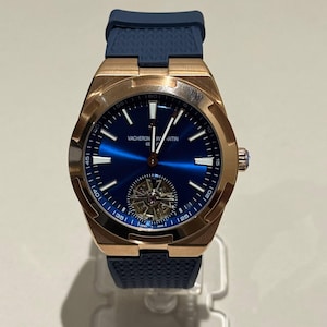 May include: A luxury wristwatch with a blue dial and a rose gold case. The watch features a blue rubber strap and a visible intricate movement. The watch face displays the brand name "VACHERON CONSTANTIN".