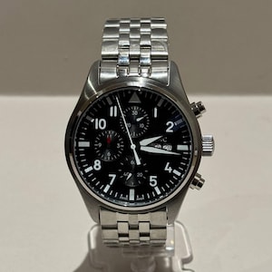 May include: A stainless steel wristwatch with a black dial. The watch features white numerals, hands, and markers. The watch has a date display and a chronograph function. The watch is on a stainless steel bracelet.