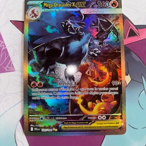 Peut inclure: Carte Pokémon holographique avec Méga-Dracaufeu X. L'illustration montre un Dracaufeu flamboyant en orange et noir, avec du texte en français. La carte est de niveau 2 et a une valeur de 360 PV.