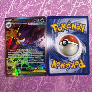 Op de afbeelding: Twee ruilkaarten, waaronder een Mega Ectoplasma EX-kaart met een paars spookfiguur en een standaard Pokemon-kaart met een blauwe achterkant en een rood-witte balafbeelding. De kaarten bevatten Franstalige tekst en spelstatistieken.