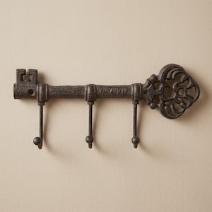 May include: A cast iron key-shaped wall hook with three hooks. The key has an ornate design on the head and the word "TOLIMA" is visible on the shaft. The finish is a dark, rustic color.