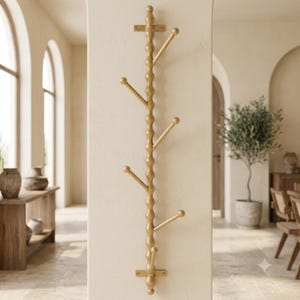 May include: A vertical wall-mounted coat rack with a gold finish, featuring a central beaded rod and six angled hooks extending outward. The rack is secured to the wall with two flat metal brackets at the top and bottom, providing a functional storage solution.