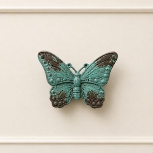 May include: A decorative butterfly with a distressed, aged appearance. The butterfly is teal with brown accents on the wings. The butterfly is made of metal and has a detailed design.
