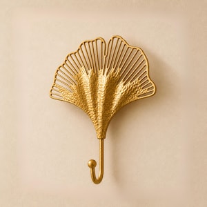 May include: A gold-colored metal wall hook in the shape of a ginkgo leaf. The hook has a textured surface and a curved hook at the bottom. The ginkgo leaf design features a fan-like shape with detailed lines.
