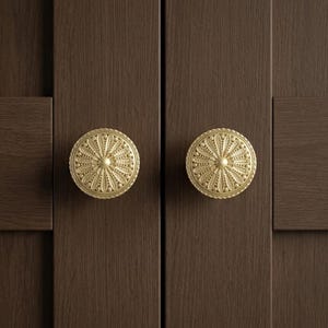 May include: Two circular cabinet knobs with a matte gold finish and a detailed, embossed floral petal pattern radiating from a central point. The knobs are mounted on a dark brown cabinet door with a visible vertical wood grain texture.