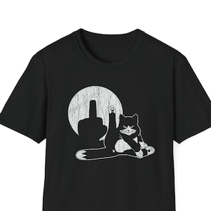 May include: A black short-sleeve t-shirt featuring a white graphic print of a cat sitting with one leg raised. Behind the cat is a distressed circular moon shape with a silhouette of a hand making a middle finger gesture in the center.