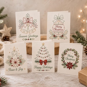 May include: Five white greeting cards featuring embroidered-style holiday designs. One shows bells with 'Season's Greetings', one a bauble with 'Merry Christmas', one a candle with 'Peace & Joy', one a tree with 'Happy Holidays', and one a wreath with 'Merry Christmas'.