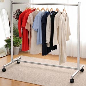 Pode incluir: Um cabideiro com rodas de metal prateado, exibindo uma variedade de roupas em cabides de madeira. As roupas incluem itens vermelhos, bege, azuis, azul marinho, pretos e creme. O cabideiro está sobre um tapete bege.