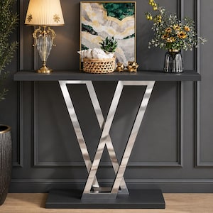 Può includere: Una consolle moderna con piano e base grigio scuro, sostenuta da una struttura in metallo argentato lucido a forma di X. Il tavolo è decorato con una lampada, opere d'arte, un cestino e un vaso di fiori. La stanza ha pareti grigio scuro.
