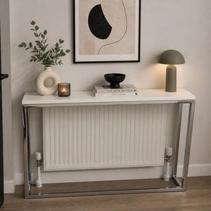 May include: A contemporary console table with a white surface and a chrome frame. It features a white vase with foliage, a candle, a black bowl, books, and a green mushroom lamp. The table is 120 cm long.