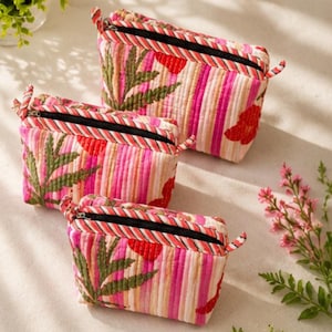 Puede incluir: Tres estuches rectangulares acolchados con un vibrante patrón de rayas rosas y blancas, motivos de hojas verdes y detalles florales rojos. Cada estuche tiene una cremallera negra con un borde de tela a rayas en la parte superior.