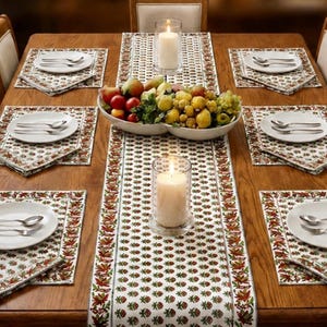 Op de afbeelding: Een houten eettafel gedekt met witte borden, bestek en placemats met patronen. Een fruitstuk en kaarsen dragen bij aan de sfeer. De tafel is gedekt voor acht personen.