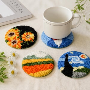 May include: Four round punch needle coasters featuring textured designs: one with yellow sunflowers on a black background, one with a blue and white pattern under a white ceramic mug, one with a landscape, and one with a swirling blue sky.