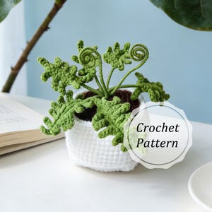 May include: A handmade crochet plant with green leaves and a spiral design, potted in a white, textured crochet pot. The text "Crochet Pattern" is visible on the image. The plant sits on a white surface.