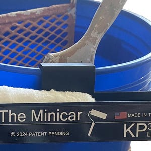 May include: A blue paint bucket with a roller tray and a paint roller. The image also shows a black tray with the text "The Minicar" and "Made in the USA". A paint roller is placed in the tray.