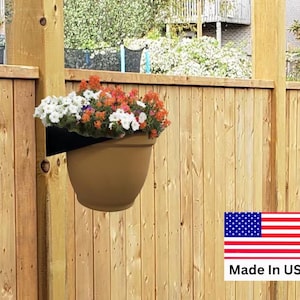 May include: A brown hanging flower pot filled with colorful flowers, mounted on a wooden fence. The flowers are a mix of white, orange, and purple. The pot is held by a black bracket. The image includes a "Made in USA" label.