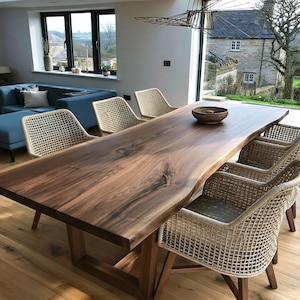 Può includere: Un grande tavolo da pranzo in legno massello con bordo naturale, sostenuto da una base in legno. Sei sedie con schienali intrecciati e telai colorati chiari circondano il tavolo. Una ciotola intrecciata è posta sul tavolo. La stanza ha un design moderno.